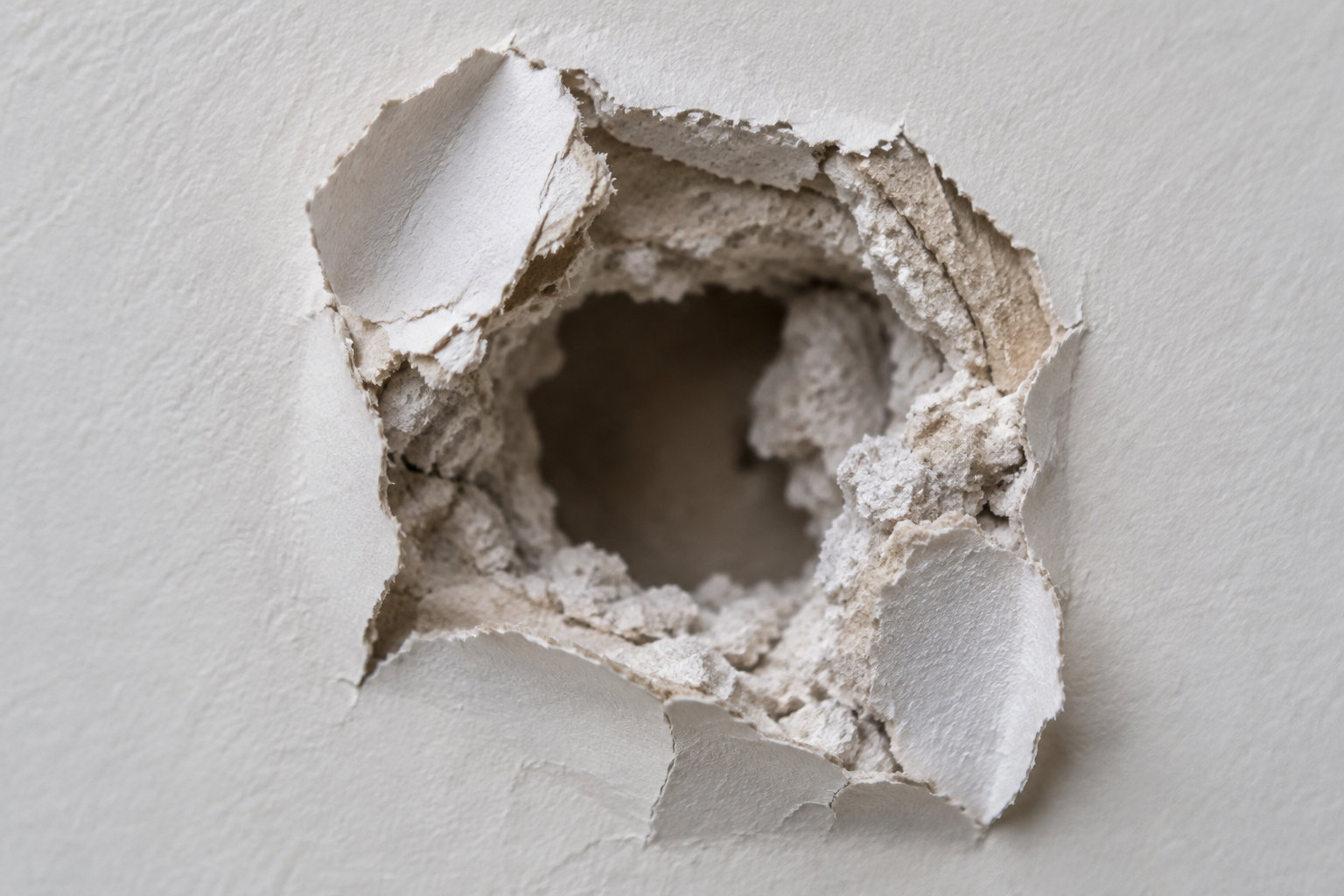 Un trou aux bords irréguliers est percé dans un mur blanc en plâtre.